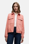 Veste courte corail de Street One, avec poches plaquées et fermeture éclair, portée sur un col roulé blanc et un jean bleu.