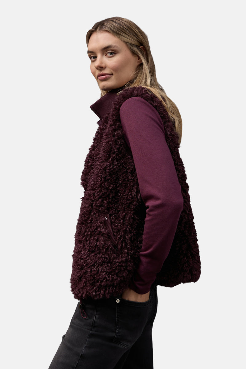 Gilet rouge bordeaux en fausse fourrure de Street One, porté sur un pull bordeaux et un jean noir.
