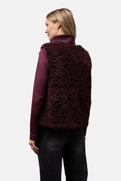 Gilet rouge en fourrure de STREET ONE, porté sur un col roulé bordeaux et un jean noir délavé, vue de dos.
