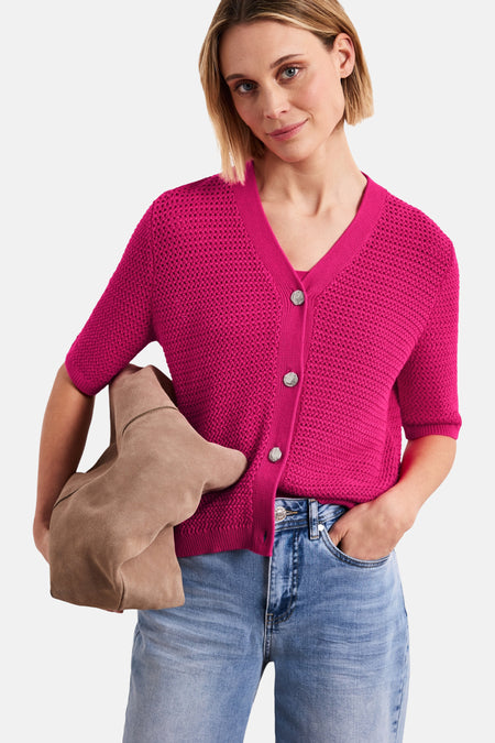 Fuchsia roze vest van getextureerd breiwerk van STREET ONE met korte mouwen, V-hals en knopen, gedragen met een lichte jeans, beige muiltjes en een suède tas.