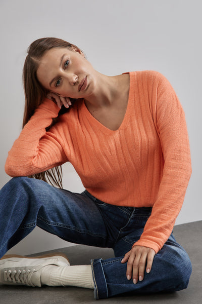 Oranje trui met V van STREET ONE, in gareel, gedragen met een blauwe jeans en witte sneakers.