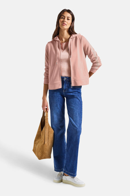 Roze Street One sweatvest met rits en capuchon, gedragen over een T-shirt en een blauwe jeans.