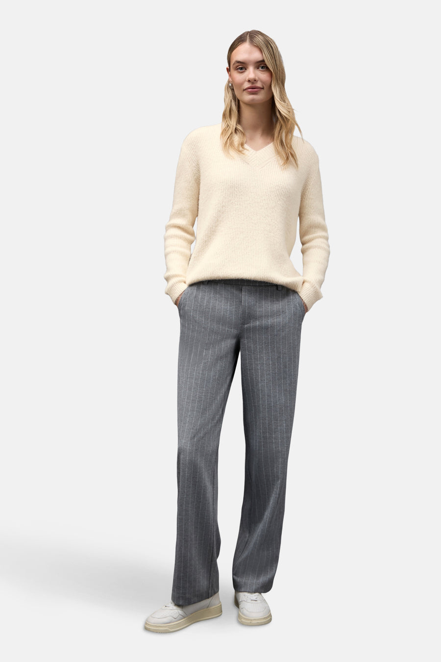 Pull col V écru de Street One, porté avec un pantalon rayé gris et des baskets blanches.
