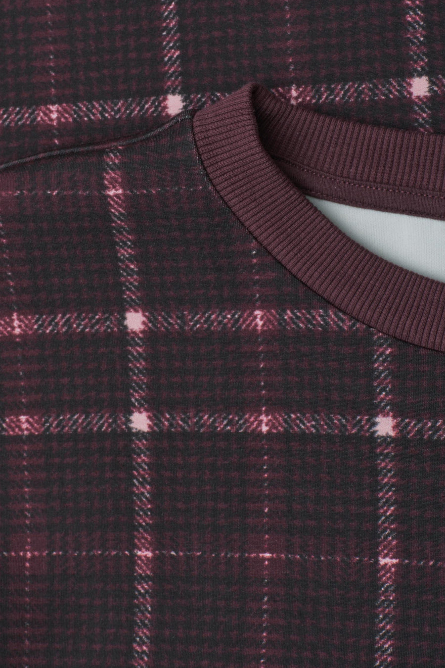 Multicolored plaid sweatshirt with ribbed crew neckline, close-up view showing dark maroon and black checkered pattern with pink accents