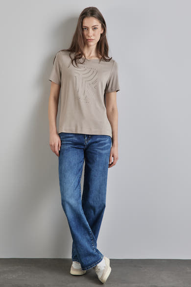 Top uni manches courtes beige de Street One avec motif décoratif sur le devant, porté avec un jean bleu et des baskets.
