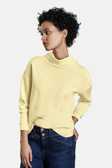 Gele sweater, van STREET ONE, met reliëftekstpatroon, gedragen met een blauwe jeans en witte sneakers.