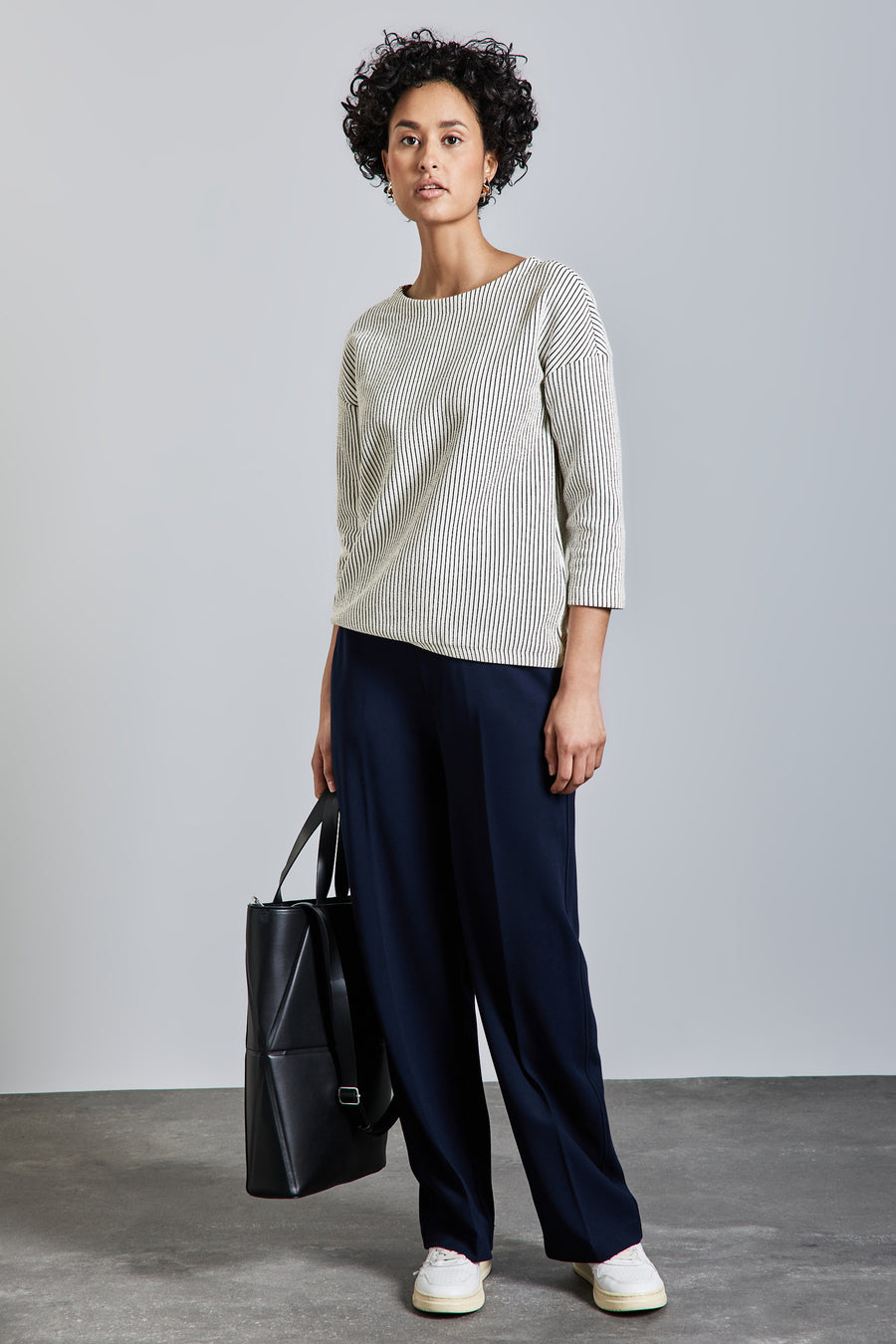 T-shirt à manches longues blanc rayé noir de Street One, porté avec un pantalon bleu marine ample et un sac noir.
