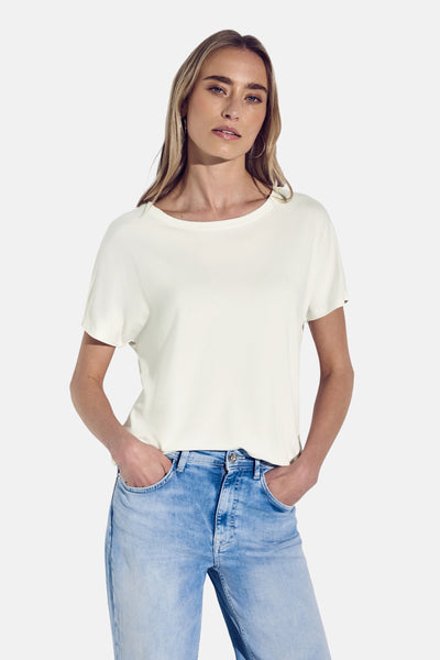 Top street one korte mouwen in ecru, gedragen met een lichte blauwe jeans, handen in de zakken.