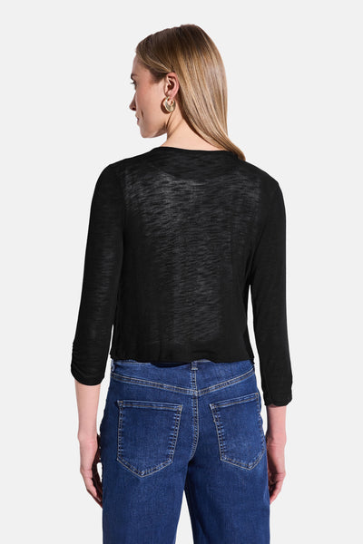 Zwarte doorschijnende gebreide bodywarmer Street One, gedragen met een high-waisted jeans en gouden oorbellen.