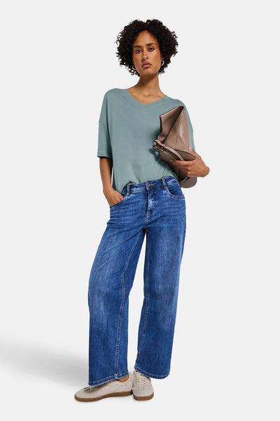 Street One blauwe V-hals trui, gedragen met een wijde jeans en een taupekleurige leren handtas.