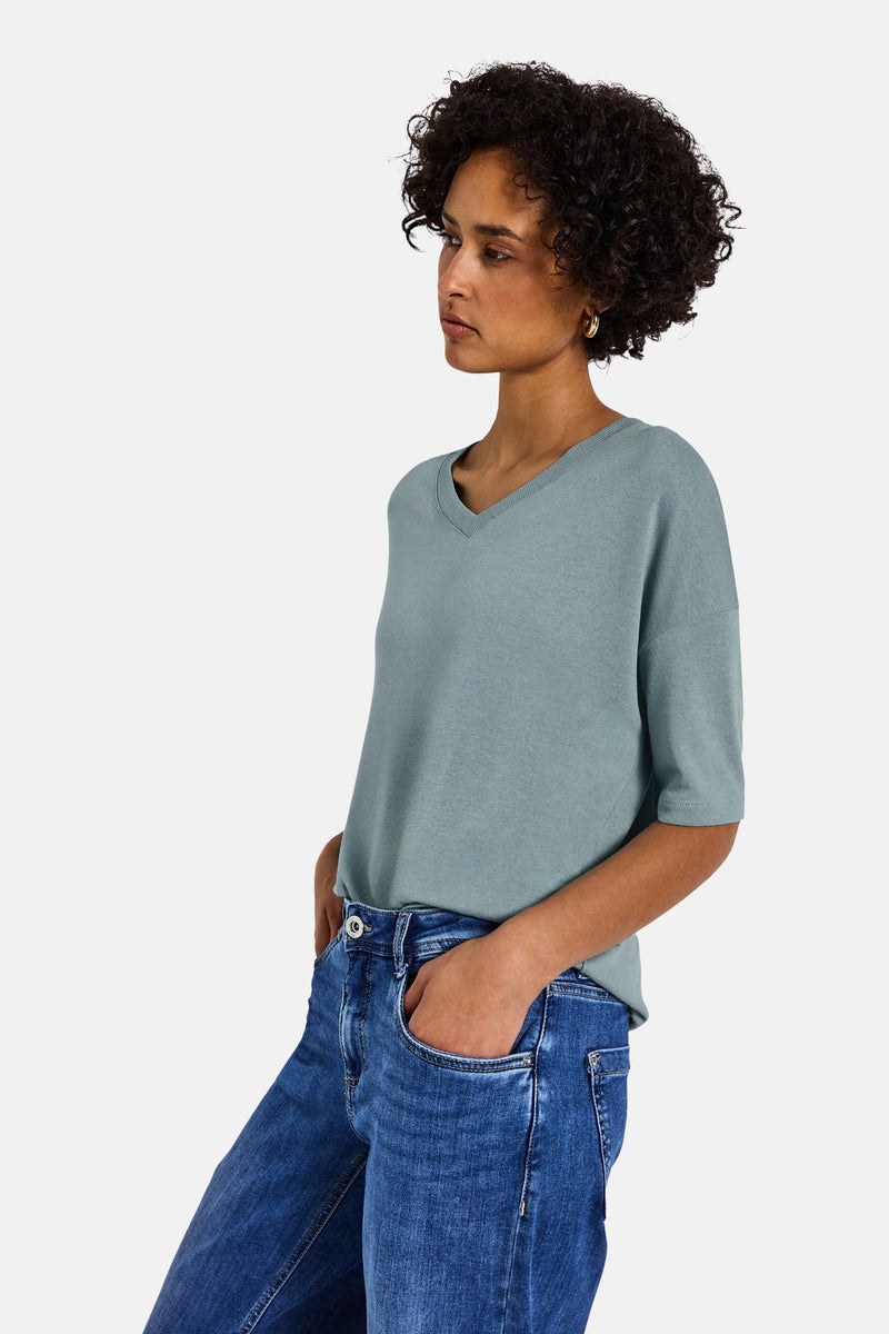 V-hals trui blauw van STREET ONE, gedragen met een spijkerbroek, met gouden oorbellen.