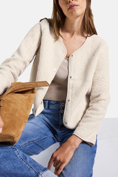 Ecru gilet van Street One, met een bouclé textuur, gedragen over een hemdje, met een blauwe jeans en een bruine tas.