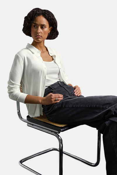 Top met lange mouwen wit van Street One gedragen met een zwarte jeans, zittend op een designstoel.