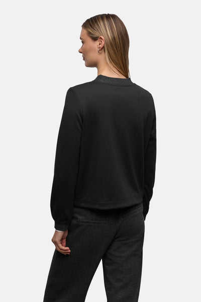 Gilet noir de STREET ONE, avec des détails scintillants au col et porté avec un pantalon gris foncé.