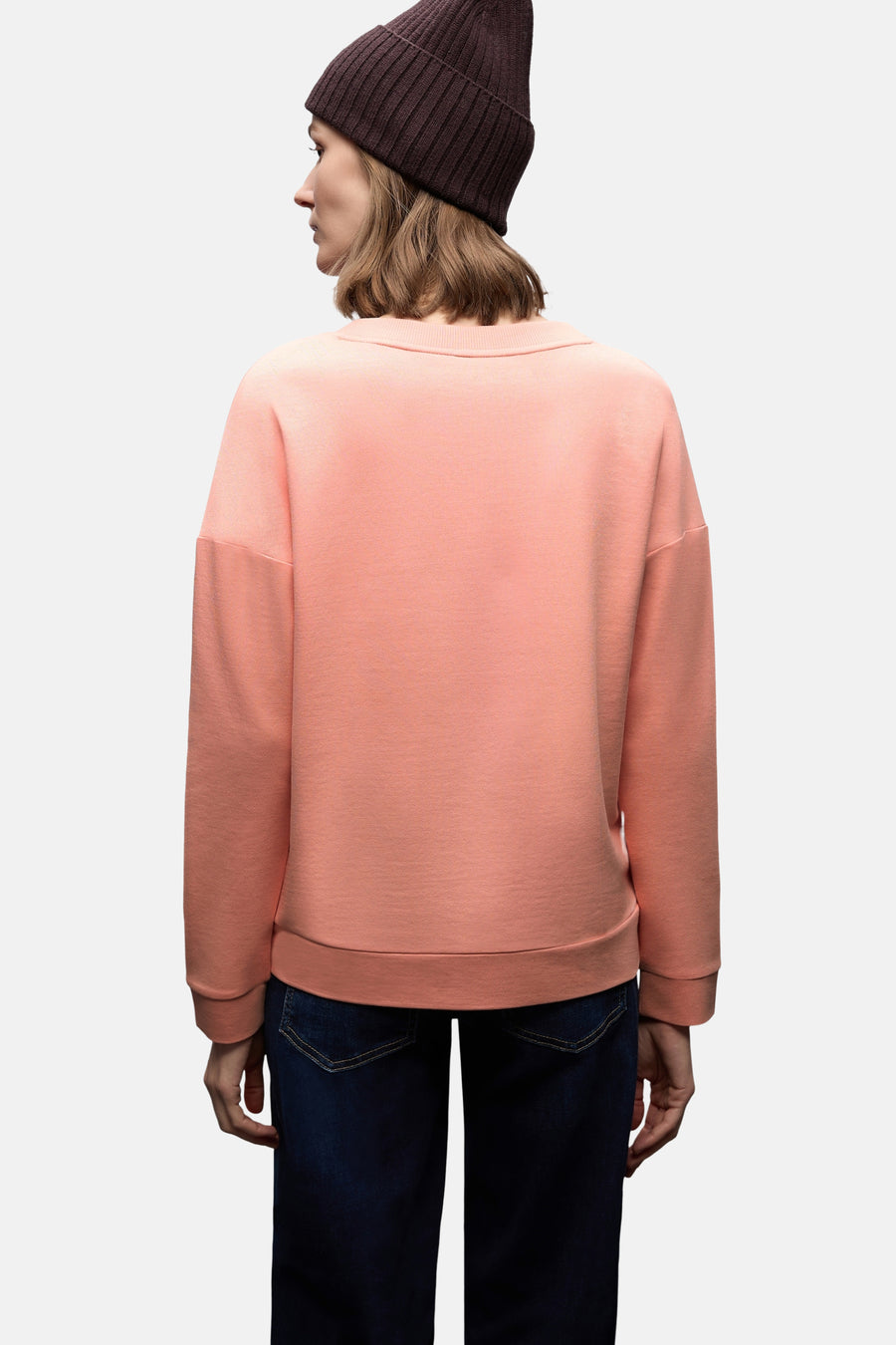 Sweat col rond corail de STREET ONE, porté avec un bonnet marron et un jean bleu, vue de dos.
