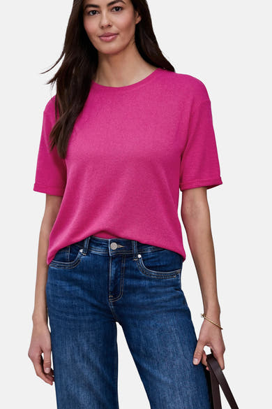 Bright pink short-sleeve ribbed T-shirt with round neckline, worn with dark blue jeans and gold bracelet, front view.