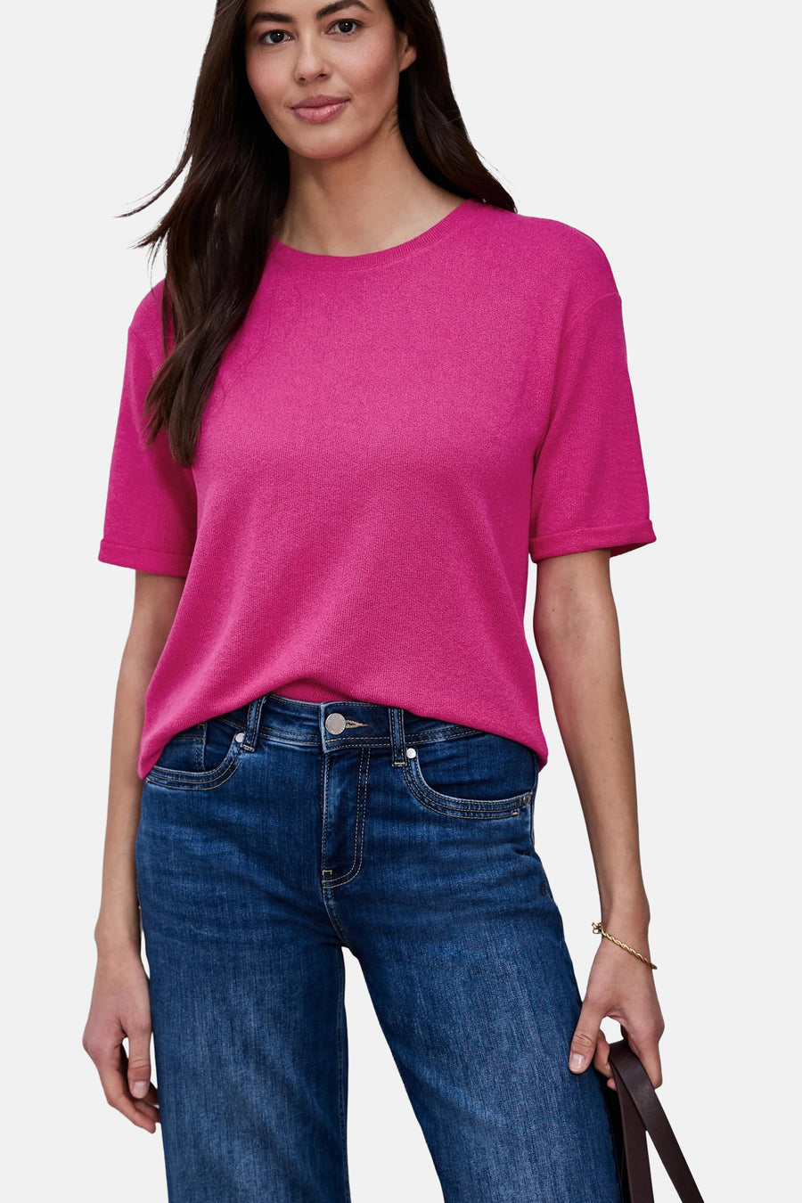 Bright pink short-sleeve ribbed T-shirt with round neckline, worn with dark blue jeans and gold bracelet, front view.