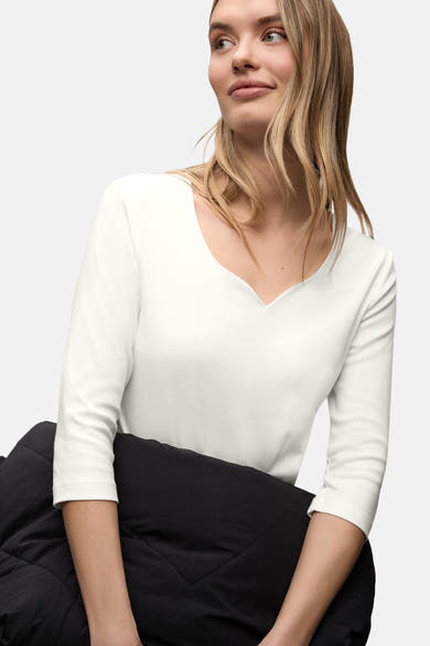 Wit T-shirt met korte mouwen van Street One, gedragen met een zwarte gewatteerde jas en blond haar dat over de schouders valt.