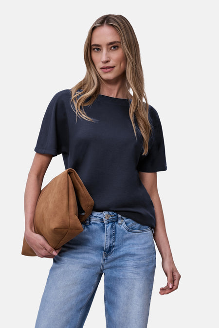 Blauw T-shirt van STREET ONE gedragen met een lichte spijkerbroek, en een bruin suède clutch vasthoudend.