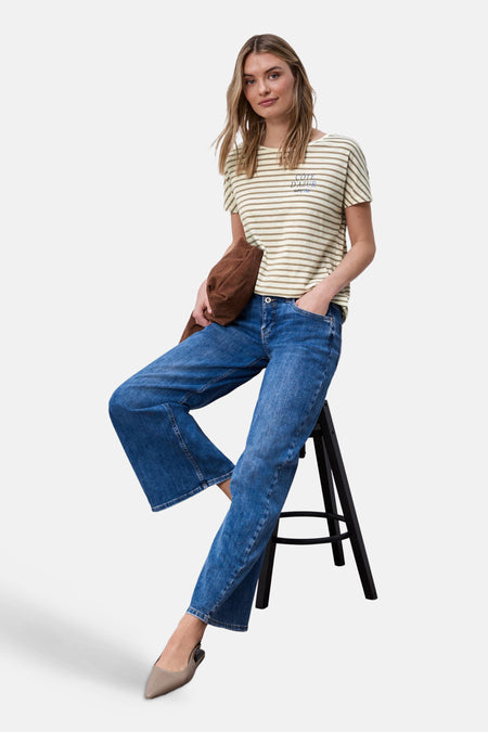 T-shirt beige à rayures par STREET ONE, porté par une femme assise sur une chaise avec un pantalon denim et des escarpins.