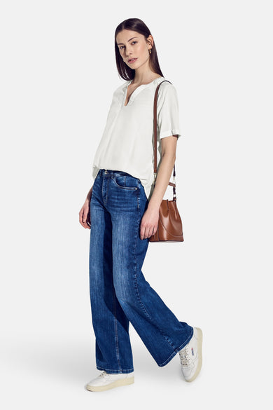 Chemisier blanc à manches courtes de Street One, porté avec un jean bleu large, un sac à main marron et des baskets blanches.
