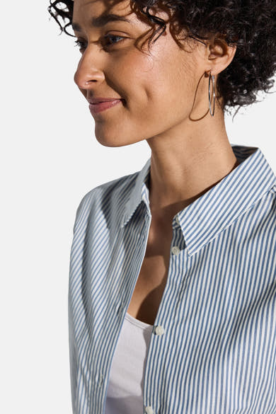 Chemisier bleu à rayures verticales de STREET ONE, porté ouvert sur un débardeur blanc, avec des boucles d'oreilles argentées.
