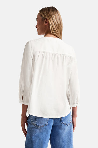 Chemisier blanc à manches longues de Street One, coupe ample avec détails froncés dans le dos, porté avec un jean.
