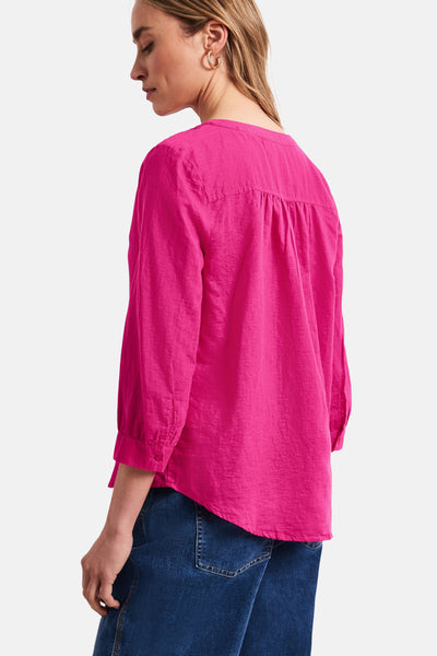 Blouse rose de STREET ONE à manches 3/4, dos froncé, portée de dos avec un jean bleu et des boucles d'oreilles dorées.