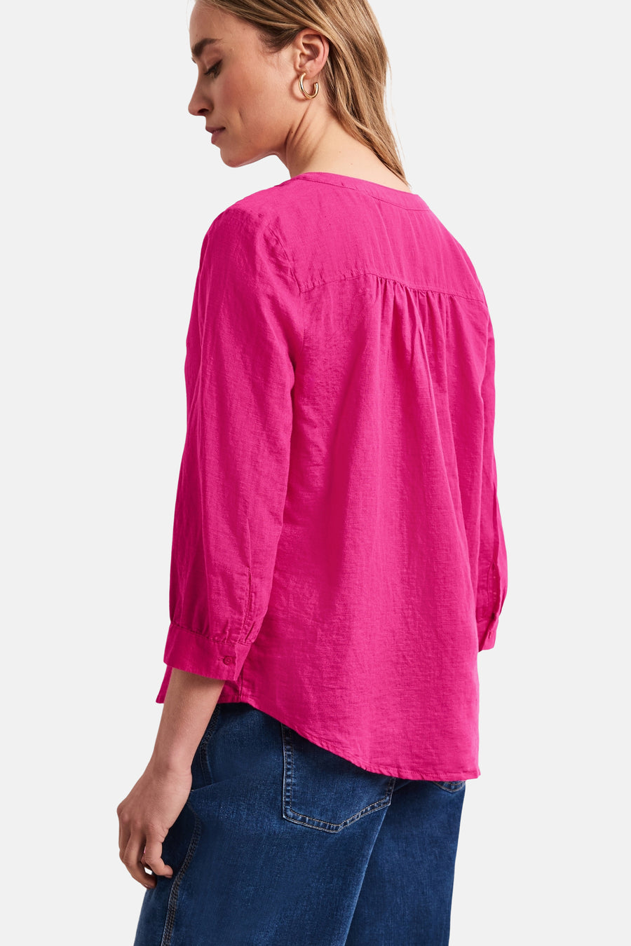 Blouse rose de STREET ONE à manches 3/4, dos froncé, portée de dos avec un jean bleu et des boucles d'oreilles dorées.