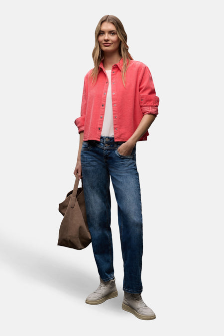 Chemise à manches longues corail par Street One, portée ouverte sur un t-shirt blanc et un jean, avec un sac en daim marron.
