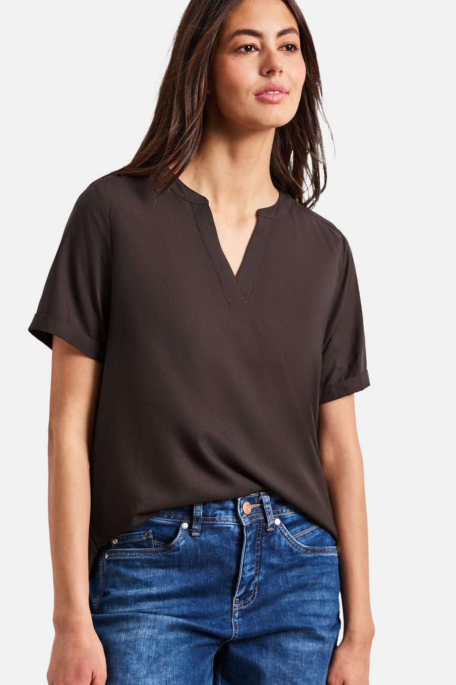 Bruine blouse van STREET ONE, open gedragen met borstzakken over een donkere top, een blauwe jeans, bruine loafers en een gestreepte tas.