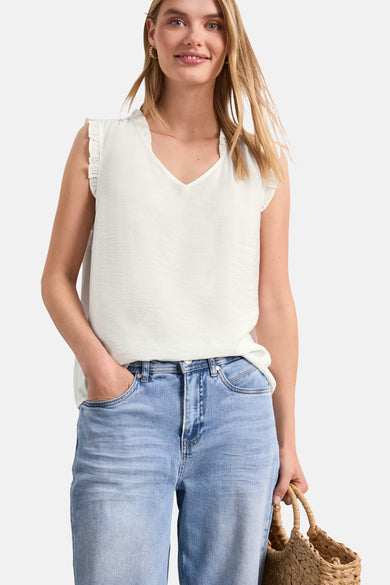 White sleeveless blouse with ruffled shoulders and V-neck, worn with light blue jeans and a woven tote bag, front view.