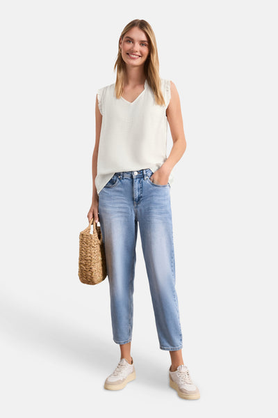 White sleeveless blouse with V-neck and ruffled shoulders, worn with light blue jeans and beige sneakers, full-length lifestyle view