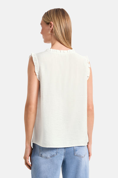 White sleeveless blouse with ruffled shoulders and gathered neckline, back view, worn with light blue jeans