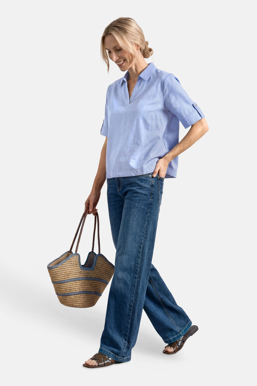Light blue short-sleeve blouse with rolled cuffs and V-neck, worn with wide-leg jeans and brown sandals, side view lifestyle pose