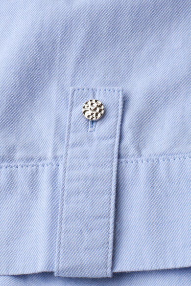 Light blue short-sleeve blouse with fine twill texture and decorative silver button on cuff, close-up detail