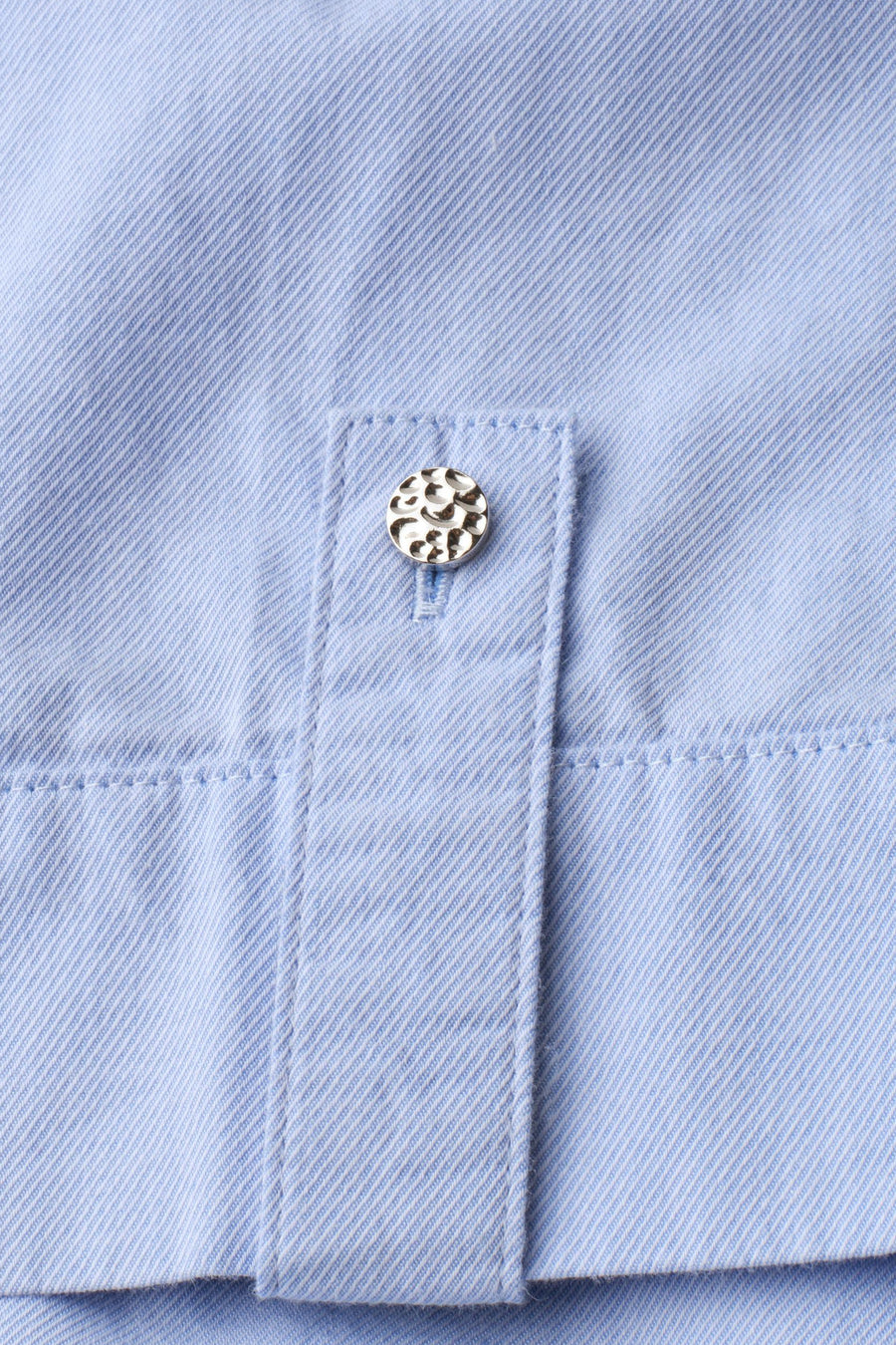 Light blue short-sleeve blouse with fine twill texture and decorative silver button on cuff, close-up detail