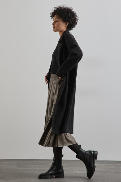 Lange beige rok van STREET ONE, geplooid met een zwarte jas, gedragen met een zwarte panty en laarzen.