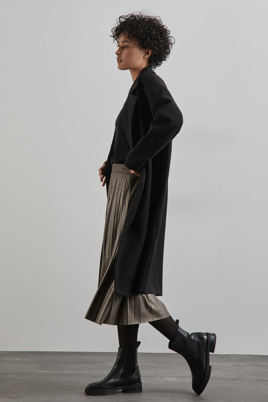 Lange beige rok van STREET ONE, geplooid met een zwarte jas, gedragen met een zwarte panty en laarzen.