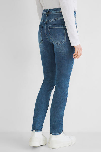 Slim-fit blue denim jeans from back view, featuring classic stitching and two rear pockets, worn with white top and sneakers.