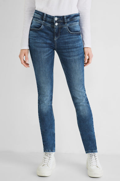 Slim-fit blue jeans with faded wash and white stitching, worn with white long-sleeve top and chunky white sneakers, front view