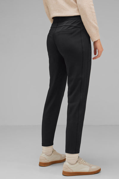 Pantalon noir de Street One, avec poches arrière, porté avec un pull beige et des baskets crème.