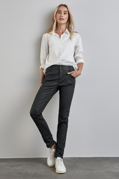 Pantalon noir de Street One, porté avec une chemise blanche et des baskets blanches, posant contre un mur gris clair.