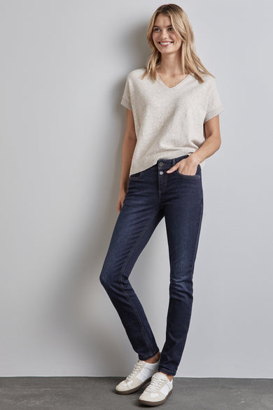 Skinny jeans in donkerblauw denim van STREET ONE, gedragen met een beige V-hals trui en witte sneakers.