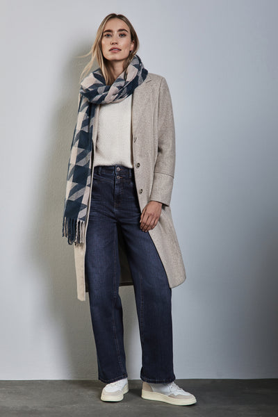 Wijde spijkerbroek in donkerblauw denim van Street One, gedragen met een crèmekleurige trui, een beige jas en een geruite sjaal.