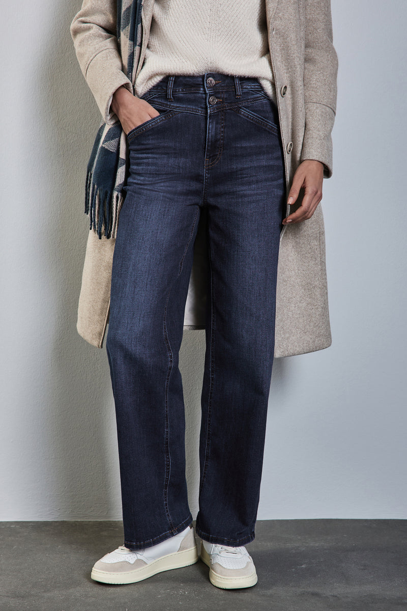 Wijde spijkerbroek in donkerblauw denim van STREET ONE, gedragen met een crèmekleurige trui, een beige jas en witte sneakers.