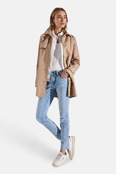 Slim jeans in lichtblauw denim van Street One, gedragen met een wit overhemd en een beige trenchcoat.