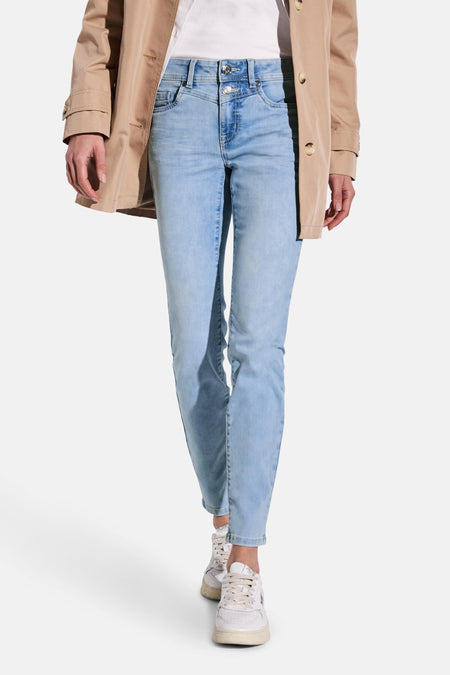 Slim jeans in lichtblauw denim van STREET ONE, gedragen met een beige trenchcoat en witte sneakers.