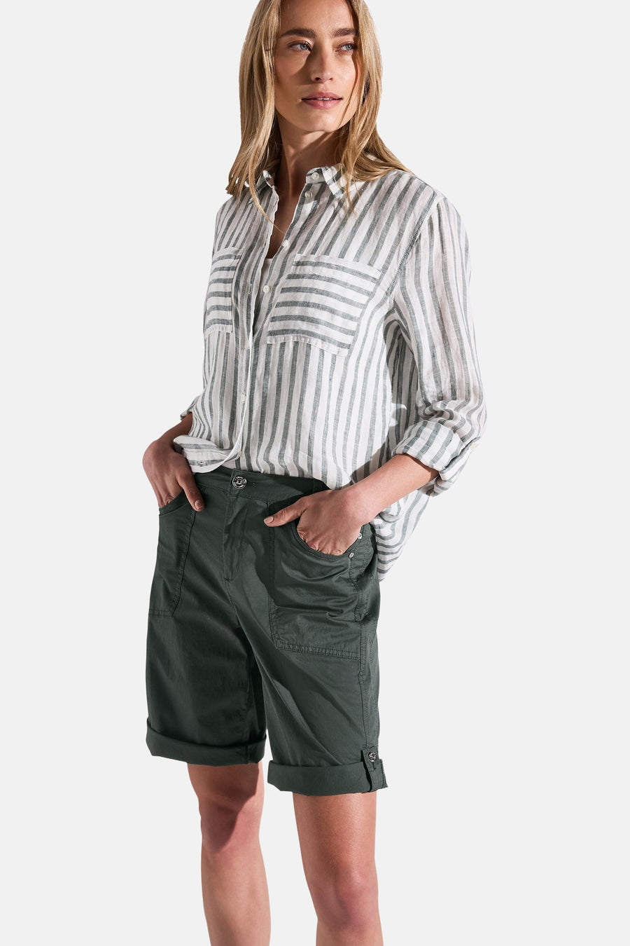 Bermuda kaki de Street One, porté avec une chemise rayée et les mains dans les poches.