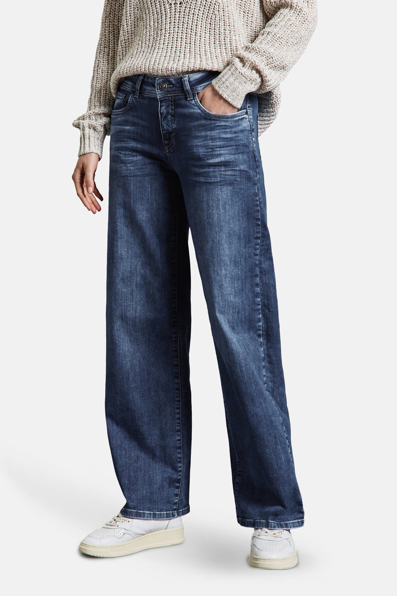 Wijde spijkerbroek in middieblauw denim van Street One, gedragen met een grofgebreide trui en witte sneakers.